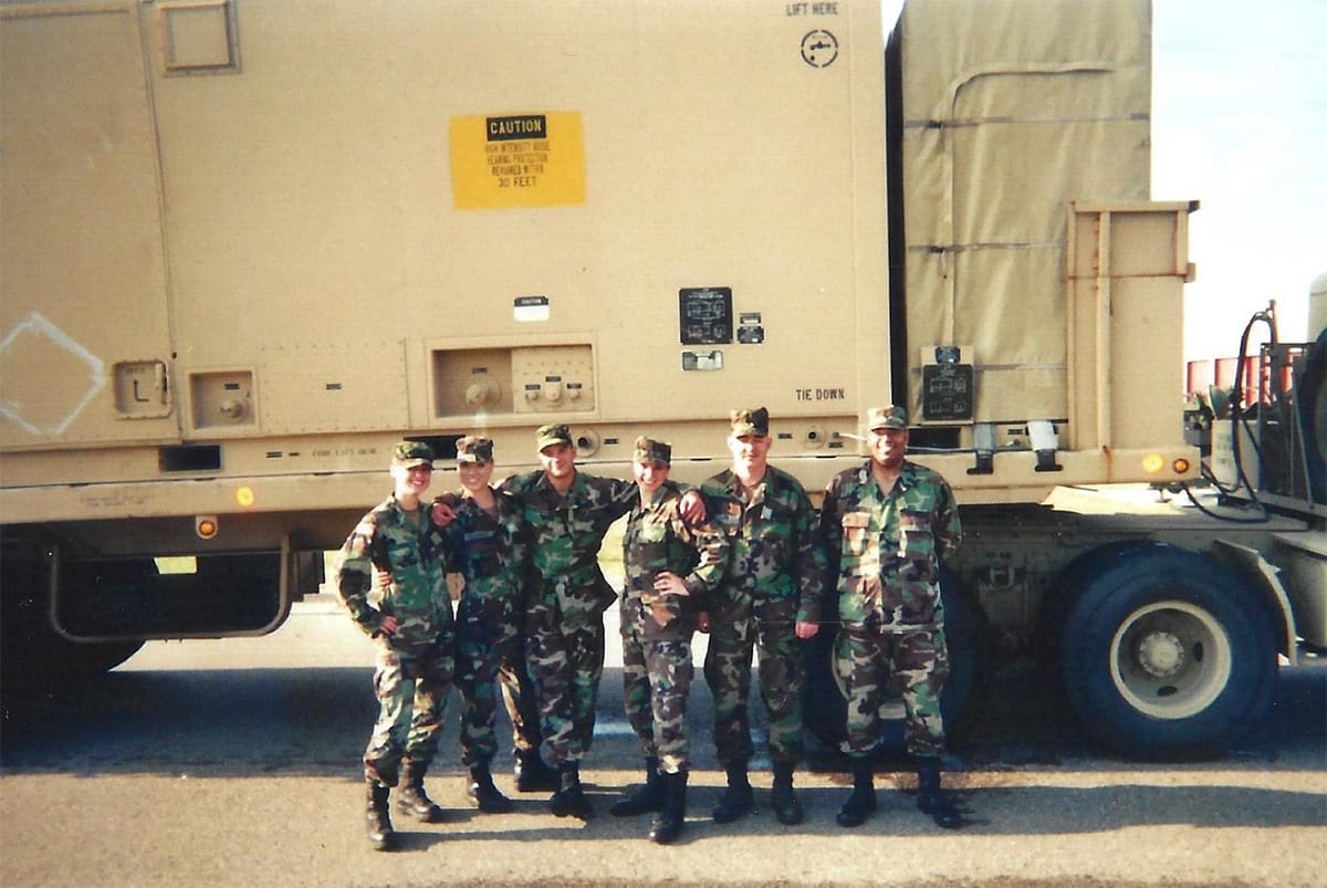Photo of Kristy and her fellow Army soliders on active duty, wearing combat fatigues in front of a large truck.